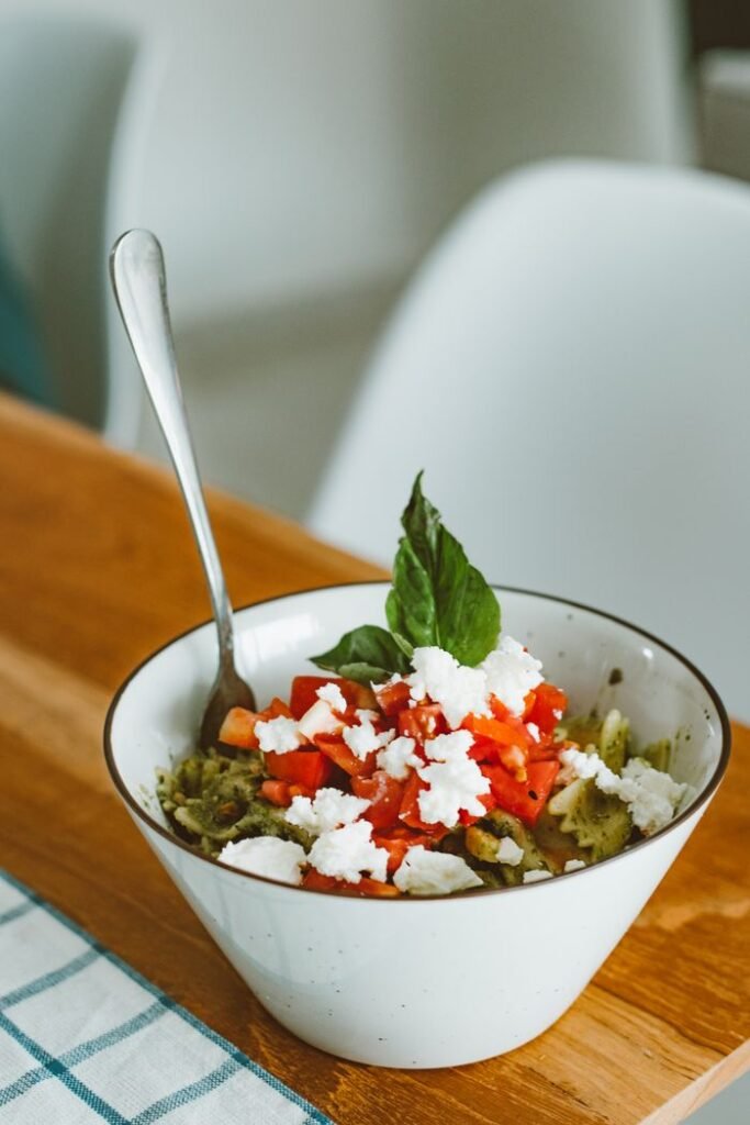 Bowl of tasty basil pesto pasta garnished with fresh tomatoes and feta cheese, perfect for Italian cuisine lovers.