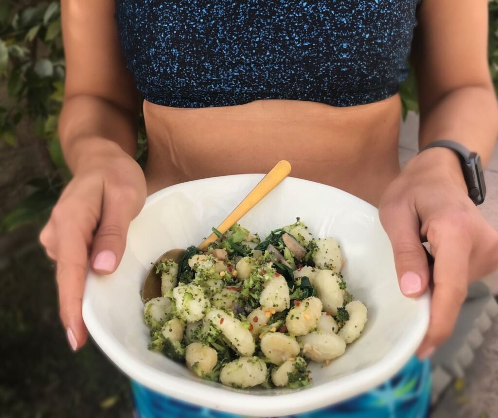 Woman in athletic wear holding a healthy gnocchi bowl, perfect for a nutritious meal.